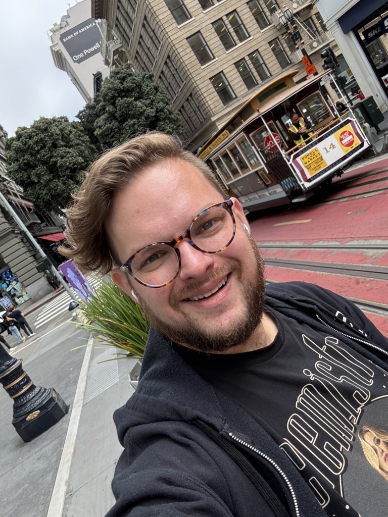 Selfie at Powell Street with a cable car and the One Powell sign visible in the background